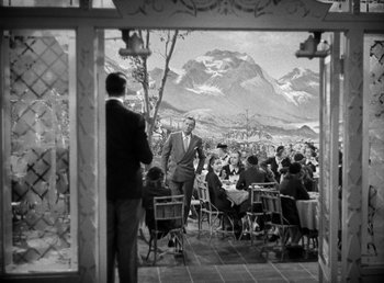 Movie still from “Mad About Music” (1938), directed by Norman Taurog – An old black and white photo of people sitting at tables in front of mountains; Wide shot, Over the shoulder angle