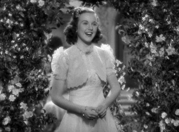 Movie still from “Mad About Music” (1938), directed by Norman Taurog – A woman in a white dress standing next to a bush; Medium shot, Low angle