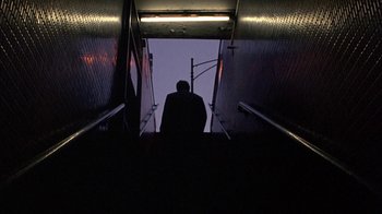 Movie still from “Mad Dog and Glory” (1993), directed by John McNaughton – A man is standing on a staircase in the dark; Extreme Wide shot, Low angle