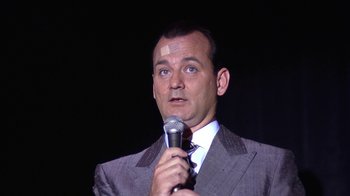 Movie still from “Mad Dog and Glory” (1993), directed by John McNaughton – A man in a suit and tie holding a microphone; Close Up shot, Low angle