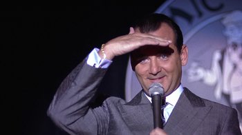 Movie still from “Mad Dog and Glory” (1993), directed by John McNaughton – A man holding a microphone up to his head; Close Up shot, Over the shoulder angle