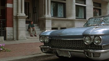 Movie still from “Mad Dog and Glory” (1993), directed by John McNaughton – A man sitting on the steps next to an old car; Wide shot, Over the shoulder angle