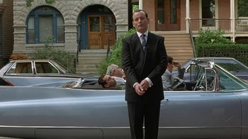 Movie still from “Mad Dog and Glory” (1993), directed by John McNaughton – A man in a suit and tie standing in front of a car; Wide shot, Low angle