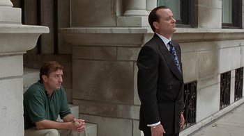 Movie still from “Mad Dog and Glory” (1993), directed by John McNaughton – A man in a business suit and tie standing next to another man in a green shirt; Medium shot, Low angle