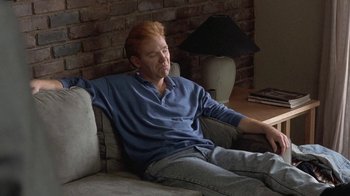 Movie still from “Mad Dog and Glory” (1993), directed by John McNaughton – A man sitting on top of a couch in a living room; Medium shot, High angle