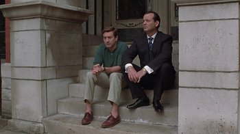 Movie still from “Mad Dog and Glory” (1993), directed by John McNaughton – A couple of men sitting next to each other on some steps; Medium shot, Low angle