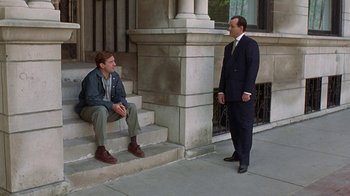 Movie still from “Mad Dog and Glory” (1993), directed by John McNaughton – A man in a suit standing on steps next to another man; Wide shot, Over the shoulder angle