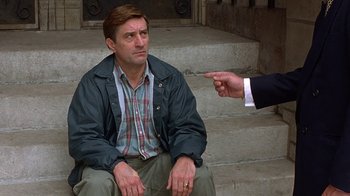 Movie still from “Mad Dog and Glory” (1993), directed by John McNaughton – A man sitting on the steps of a building with another man pointing at him; Medium shot, Over the shoulder angle