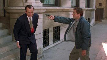 Movie still from “Mad Dog and Glory” (1993), directed by John McNaughton – A man is holding a gun pointed at a man in a suit and tie; Medium shot, Over the shoulder angle