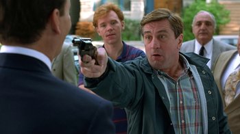 Movie still from “Mad Dog and Glory” (1993), directed by John McNaughton – A man pointing a gun at another man in front of another man; Medium shot, Over the shoulder angle