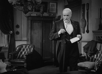 Movie still from “Madame Curie” (1943), directed by Mervyn LeRoy – An older man in a suit and tie holding a phone; Medium shot, Over the shoulder angle