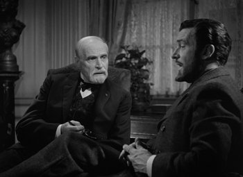 Movie still from “Madame Curie” (1943), directed by Mervyn LeRoy – Two men sitting on a couch talking to each other; Medium shot, Over the shoulder angle