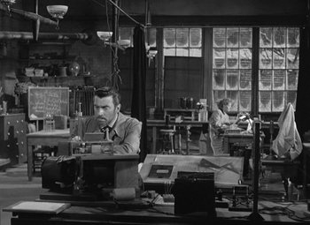 Movie still from “Madame Curie” (1943), directed by Mervyn LeRoy – A man sitting at a table in a room; Wide shot, High angle