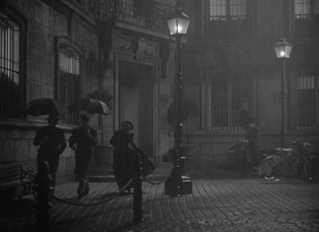 Movie still from “Madame Curie” (1943), directed by Mervyn LeRoy – A group of people walking down a street with umbrellas; Extreme Wide shot, High angle