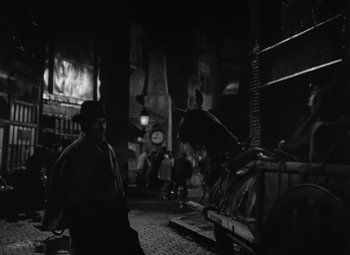 Movie still from “Madame Curie” (1943), directed by Mervyn LeRoy – A man standing next to a horse in a dark alley; Wide shot, High angle