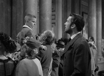 Movie still from “Madame Curie” (1943), directed by Mervyn LeRoy – A group of people standing next to each other in a building; Medium shot, Over the shoulder angle