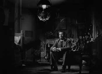 Movie still from “Madame Curie” (1943), directed by Mervyn LeRoy – A black and white photo of a man sitting in a chair; Wide shot, Low angle
