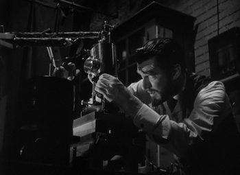 Movie still from “Madame Curie” (1943), directed by Mervyn LeRoy – A black and white photo of a man working on a machine; Medium shot, Low angle