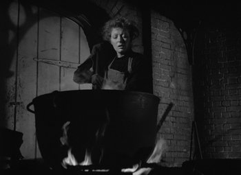 Movie still from “Madame Curie” (1943), directed by Mervyn LeRoy – A person standing in front of a pot on a fire pit; Medium shot, Low angle