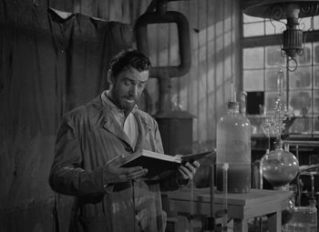 Movie still from “Madame Curie” (1943), directed by Mervyn LeRoy – A black and white photo of a man reading a book; Medium shot, Low angle
