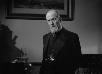 Movie still from “Madame Curie” (1943), directed by Mervyn LeRoy – An older man in a suit and tie in front of a painting; Medium shot, Low angle