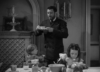 Movie still from “Madame Curie” (1943), directed by Mervyn LeRoy – A black and white photo of a man and two children at a dinner table; Medium shot, Over the shoulder angle