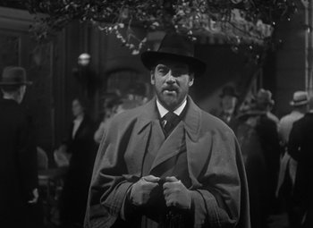 Movie still from “Madame Curie” (1943), directed by Mervyn LeRoy – A black and white photo of a man wearing a hat and a coat; Medium shot, Over the shoulder angle