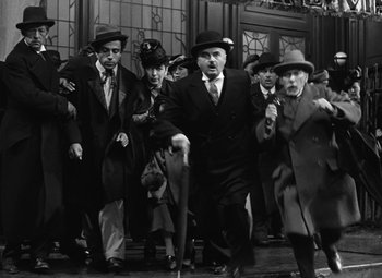 Movie still from “Madame Curie” (1943), directed by Mervyn LeRoy – A black and white photo of a group of men in suits and hats; Wide shot, High angle