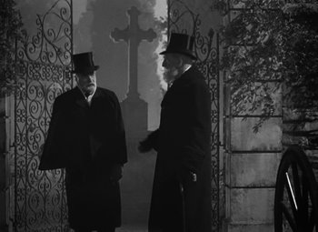 Movie still from “Madame Curie” (1943), directed by Mervyn LeRoy – Two men standing next to each other in front of a cross; Medium shot, Over the shoulder angle