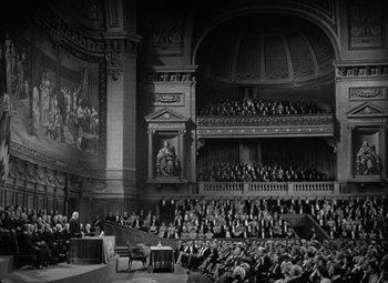 Movie still from “Madame Curie” (1943), directed by Mervyn LeRoy – An old photo of a concert hall with a large crowd of people; Extreme Wide shot, High angle