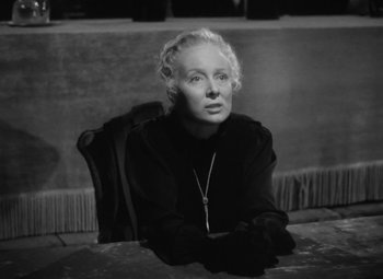 Movie still from “Madame Curie” (1943), directed by Mervyn LeRoy – An older woman sitting at a table in front of a wall; Close Up shot, Over the shoulder angle
