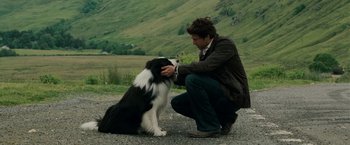 A man kneeling down next to a black and white dog