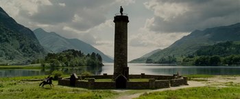 A stone tower with a statue on top of it near a body of water