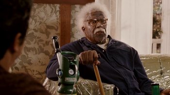 Movie still from “Madea Goes to Jail” (2009), directed by Tyler Perry – An older man sitting in front of a green fire hydrant; Medium shot, High angle