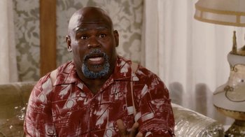 Movie still from “Madea Goes to Jail” (2009), directed by Tyler Perry – A man in a red shirt is sitting on a couch; Medium shot, High angle