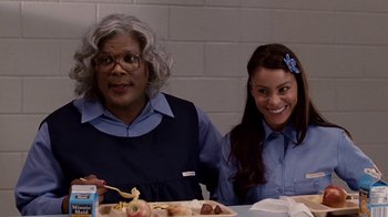 Movie still from “Madea Goes to Jail” (2009), directed by Tyler Perry – Two people sitting at a table with plates of food in front of a brick wall; Medium shot, Over the shoulder angle