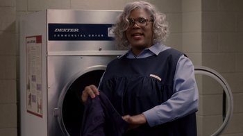 Movie still from “Madea Goes to Jail” (2009), directed by Tyler Perry – A woman holding a towel in front of a washing machine; Medium shot, Over the shoulder angle