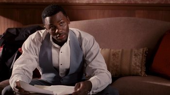 Movie still from “Madea Goes to Jail” (2009), directed by Tyler Perry – A man sitting on a couch holding a book; Medium shot, High angle