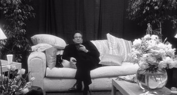 Movie still from “Madonna: Truth or Dare” (1991), directed by Alek Keshishian – A man sitting on a couch holding a remote control; Medium shot, High angle
