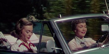 Movie still from “Magnificent Obsession” (1954), directed by Douglas Sirk – Two women in the back seat of a vintage car; Medium shot, Low angle