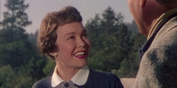 Movie still from “Magnificent Obsession” (1954), directed by Douglas Sirk – An older woman smiling at the camera in front of trees; Close Up shot, Over the shoulder angle