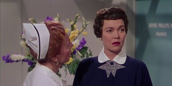 Movie still from “Magnificent Obsession” (1954), directed by Douglas Sirk – A woman in a white hat standing next to another woman in a blue dress; Close Up shot, Over the shoulder angle