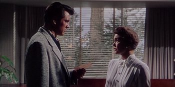 Movie still from “Magnificent Obsession” (1954), directed by Douglas Sirk – A man and a woman are standing next to each other in front of a window; Medium shot, Low angle