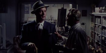 Movie still from “Magnificent Obsession” (1954), directed by Douglas Sirk – A man wearing a suit and a hat talking to another man; Medium shot, Over the shoulder angle
