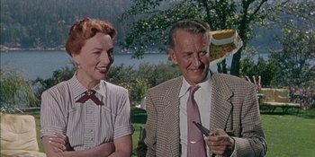 Movie still from “Magnificent Obsession” (1954), directed by Douglas Sirk – An older man and a younger woman smile at the camera; Medium shot, High angle