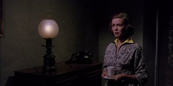 Movie still from “Magnificent Obsession” (1954), directed by Douglas Sirk – A woman standing in front of an electric lamp holding a coffee cup; Medium shot, Low angle