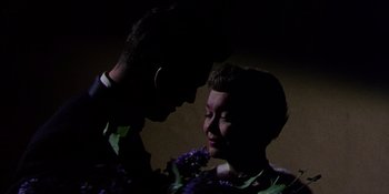 Movie still from “Magnificent Obsession” (1954), directed by Douglas Sirk – A man and a woman holding a purple flower in a dark room; Close Up shot, Low angle