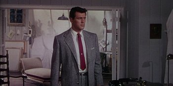 Movie still from “Magnificent Obsession” (1954), directed by Douglas Sirk – A man in a suit and tie standing next to a car; Medium shot, Low angle