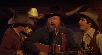 Movie still from “Making Love” (1982), directed by Arthur Hiller – A man in a cowboy hat sings into a microphone; Medium shot, Over the shoulder angle