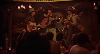 Movie still from “Making Love” (1982), directed by Arthur Hiller – A group of men in cowboy hats playing guitars; Wide shot, Over the shoulder angle